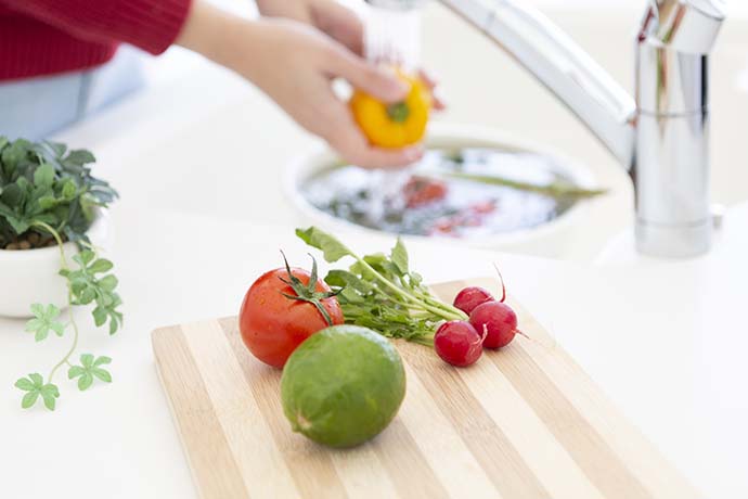 まな板の上に置かれた野菜と野菜を洗う女性